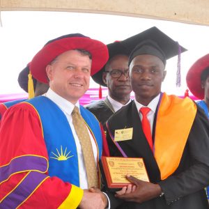 Prof. Philp Laird, Ph.D. of TWU shaking hands with a first class student from the Faculty of Education (then) on the 13th Graduation Ceremony- 13/10/2017, right is VC, Prof. Maud Kamatenesi Mugisha Ph.D.